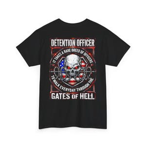 May include: A black t-shirt featuring a graphic on the back with a skull, barbed wire, and an American flag background. The text reads: DETENTION OFFICER, IT TAKES A RARE BREED OF OFFICERS TO WALK EVERYDAY THROUGH THE GATES OF HELL.