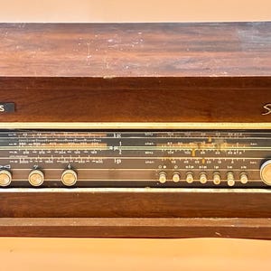 May include: Vintage Philips stereo radio with a dark wood cabinet. The radio features a black and gold face with various dials, knobs, and a tuning dial. The word "Philips" is displayed on the front, along with the word "Stereo".