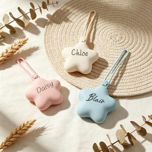 May include: Three star-shaped silicone bag tags with attached loops. One tag is cream with the name Chloe, one is light pink with the name Daisy, and one is light blue with the name Blair printed in black script on the front of each item.