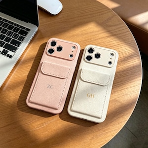May include: Two rectangular smartphone cases with integrated card pockets on the back. One case is light pink with the initials ZC, and the other is cream with the initials GH. Both feature a raised camera cutout area and a textured finish.