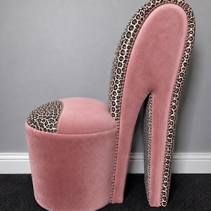 May include: A pink velvet chair in the shape of a high-heeled shoe. The heel and the top of the seat back are covered in leopard print fabric. The edges of the heel are lined with small, silver studs.