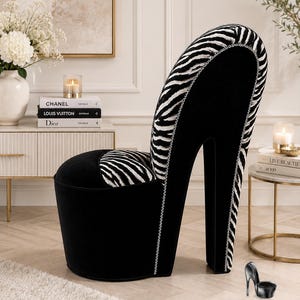 May include: A high-heel shoe shaped chair upholstered in black velvet and black and white zebra print fabric. The chair features a tall backrest, a rounded seat, and a silver nailhead trim outlining the silhouette of the heel and back.