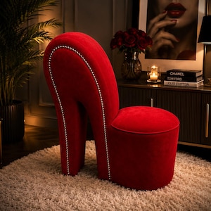 May include: A high-heeled shoe shaped chair upholstered in vibrant red velvet fabric. The backrest and heel structure are accented with a decorative trim of small, silver-toned metal studs that follow the curved silhouette of the furniture piece.