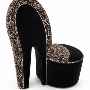 May include: A high-heel shoe shaped chair upholstered in black fabric and leopard print fabric. The design features a tall backrest and a cylindrical seat base, accented with a thin line of small, clear crystals along the seams of the upholstery.