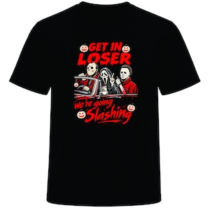 May include: A black short-sleeved t-shirt featuring a graphic of three horror movie characters in a car. The text reads GET IN LOSER and we're going SLASHING in red letters, accompanied by small orange jack-o'-lantern icons on the front.