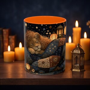 Puede incluir: Una taza cilíndrica de cerámica con interior naranja brillante y exterior oscuro que presenta una ilustración de un cachorro de león durmiendo bajo una colcha de retazos azul y marrón, rodeado de linternas brillantes y un cielo estrellado.