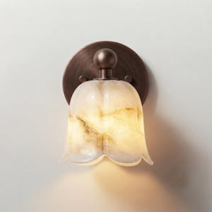 May include: A wall sconce featuring a bell-shaped, marbled glass shade with cream and amber swirls. The fixture includes a circular, brushed bronze-toned metal backplate with a central spherical accent piece connecting to the glass shade.