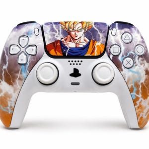 Puede incluir: Un mando de videojuegos blanco con un gráfico de un personaje rubio de pelo puntiagudo con un gi naranja en el panel táctil central. Las empuñaduras y los laterales muestran un patrón de nubes naranjas y marrones con rayos azules brillantes.