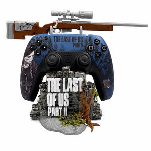 Peut inclure: Une manette PlayStation 4 bleue et noire avec un fusil au-dessus et un support avec le texte "THE LAST OF US PART II". La manette présente un motif de forêt et un portrait de femme. Le fusil est marron et argenté.