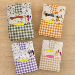 May include: Four rectangular quilted fabric pouches with snap-button closures. Each pouch features a top section with floral or fruit patterns and a bottom section with a gingham check print. The pouches contain various pens and paper inserts.