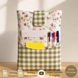 May include: A quilted fabric organizer featuring a cream background with a floral pattern and a green and white gingham check pocket. The organizer includes a flap closure, a white card labeled Focus Notes, a yellow card, and three pens.