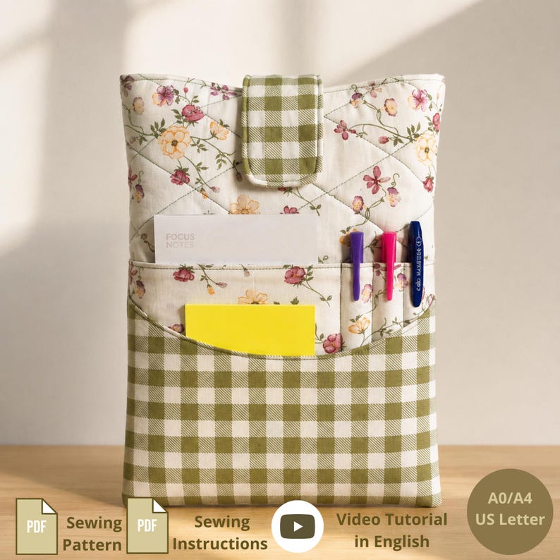 May include: A quilted fabric organizer featuring a cream background with a floral pattern and a green and white gingham check pocket. The organizer includes a flap closure, a white card labeled Focus Notes, a yellow card, and three pens.