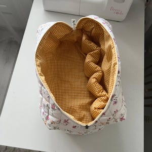 Pu&ograve; includere: Una pochette in tessuto trapuntato con esterno bianco caratterizzato da un delicato motivo floreale nei toni del rosa, arancione e verde. L'interno &egrave; foderato con un tessuto a quadretti vichy giallo e bianco. La pochette ha una chiusura a zip.