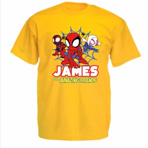 May include: A bright yellow short-sleeved t-shirt featuring a graphic of three cartoon spider-themed characters in front of a blue web. Below the characters, the text reads "JAMES AND AMAZING FRIENDS" in bold red, white, and yellow lettering.