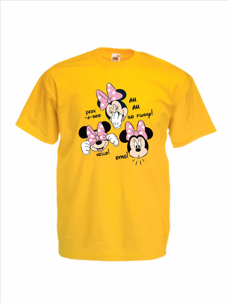 Op de afbeelding: Een gele t-shirt met drie Minnie Mouse cartoon gezichten met roze strikken. Tekst bevat "Peek-a-boo", "Hello!", "Ah ah so funny!" en "OMG!". Het shirt is gemaakt van een zacht materiaal.