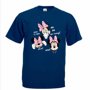 Op de afbeelding: Marineblauw T-shirt met een Minnie Mouse-ontwerp. Het ontwerp bevat Minnie Mouse met roze strikken en de zinnen "Peek-a-boo", "Hello!" en "Ah, ah, so funny!" in witte tekst. Het cartoonontwerp is gecentreerd.