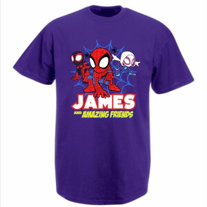 May include: A purple short-sleeved t-shirt featuring a graphic of three cartoon spider-themed characters in front of a blue web. Below the characters, the text reads JAMES AND AMAZING FRIENDS in bold white and yellow lettering on the front.