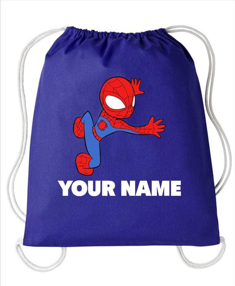 May include: A royal blue drawstring backpack featuring a cartoon illustration of a red and blue spider-themed character in a dynamic pose. Below the character, the text YOUR NAME is printed in bold white capital letters. The bag has white cords.