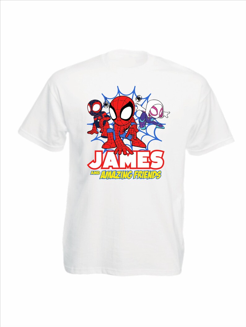 May include: A white short-sleeve t-shirt featuring a graphic of three cartoon superheroes in front of a blue spiderweb. Below the characters, the text reads "JAMES AND AMAZING FRIENDS" in red and yellow block lettering with a black outline.