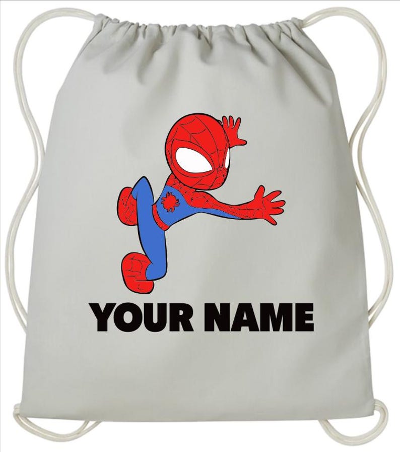 May include: A light grey drawstring backpack featuring a cartoon illustration of a red and blue superhero character in a dynamic pose. Below the character, the text "YOUR NAME" is printed in bold, black, sans-serif capital letters.