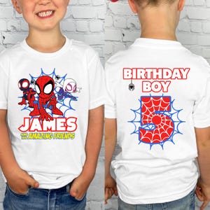 May include: A white t-shirt featuring a graphic of Spider-Man and friends with the text James and his Amazing Friends on the front, and the text Birthday Boy with a large number 5 in a spiderweb pattern on the back of the garment.