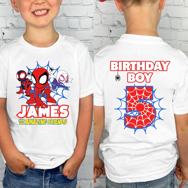 May include: A white t-shirt featuring a graphic of Spider-Man and friends with the text James and his Amazing Friends on the front, and the text Birthday Boy with a large number 5 in a spiderweb pattern on the back of the garment.