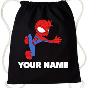 May include: A black drawstring backpack featuring a graphic of a red and blue cartoon superhero in a dynamic pose. Below the character, the text "YOUR NAME" is printed in bold white capital letters. The bag has white cord straps on both sides.