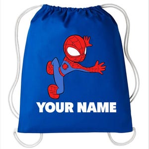 May include: A royal blue drawstring bag featuring a cartoon illustration of a red and blue superhero character in a dynamic pose. Below the character, the text "YOUR NAME" is printed in bold, white, capital letters. The bag has white cords.