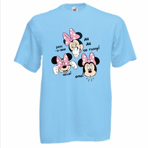 Op de afbeelding: Lichtblauw T-shirt met een Minnie Mouse-afbeelding. De afbeelding toont Minnie met roze strikken en de zinnen "Peek-a-boo", "Hello!", "Ah Ah So Funny!" en "OMG!" in zwarte tekst.