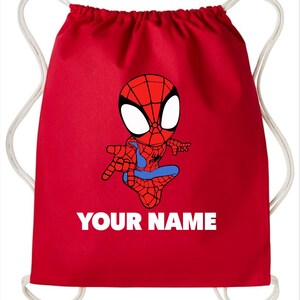May include: A bright red drawstring backpack featuring a cartoon illustration of a spider-themed superhero in a crouching pose. Below the character, the text "YOUR NAME" is printed in bold white capital letters. The bag has white cord straps.