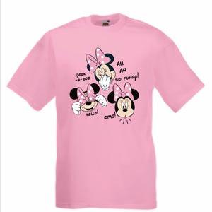 Op de afbeelding: Lichtroze T-shirt met drie Minnie Mouse-afbeeldingen met stippen strikken. Tekst bevat "Peek-a-boo", "Hello!", "Ah, ah, so funny!" en "OMG!"