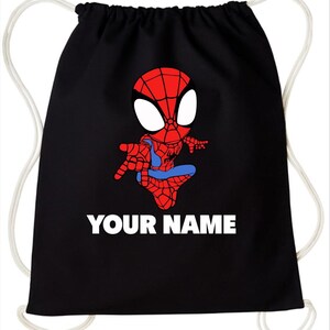 May include: A black drawstring backpack featuring a graphic of a cartoon superhero with a red and blue suit and large white eyes. Below the character, the text YOUR NAME is printed in bold white capital letters. The bag has white cord straps.