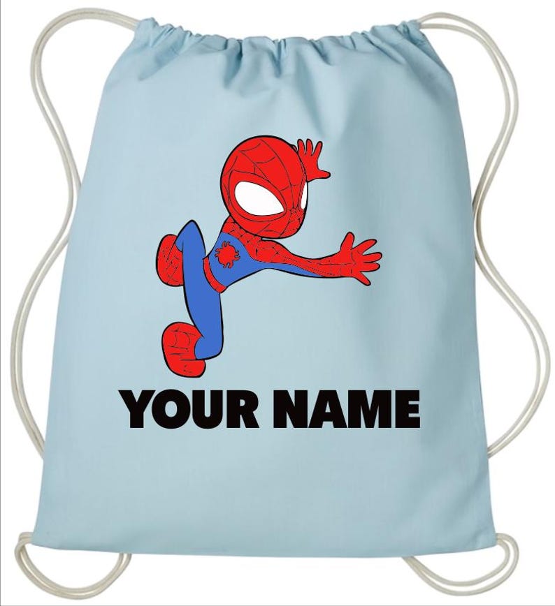 May include: A light blue drawstring backpack featuring a cartoon illustration of a red and blue superhero character in a dynamic pose. Below the character, the text YOUR NAME is printed in bold black capital letters. The bag has white cords.