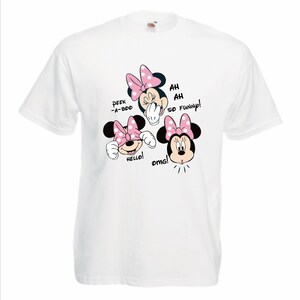 Op de afbeelding: Wit t-shirt met drie Minnie Mouse-gezichten met roze strikken. Tekst bevat "Peek-a-boo", "Hello!", "Ah Ah So Funny!" en "omg!". Het shirt is gemaakt van een zacht materiaal.