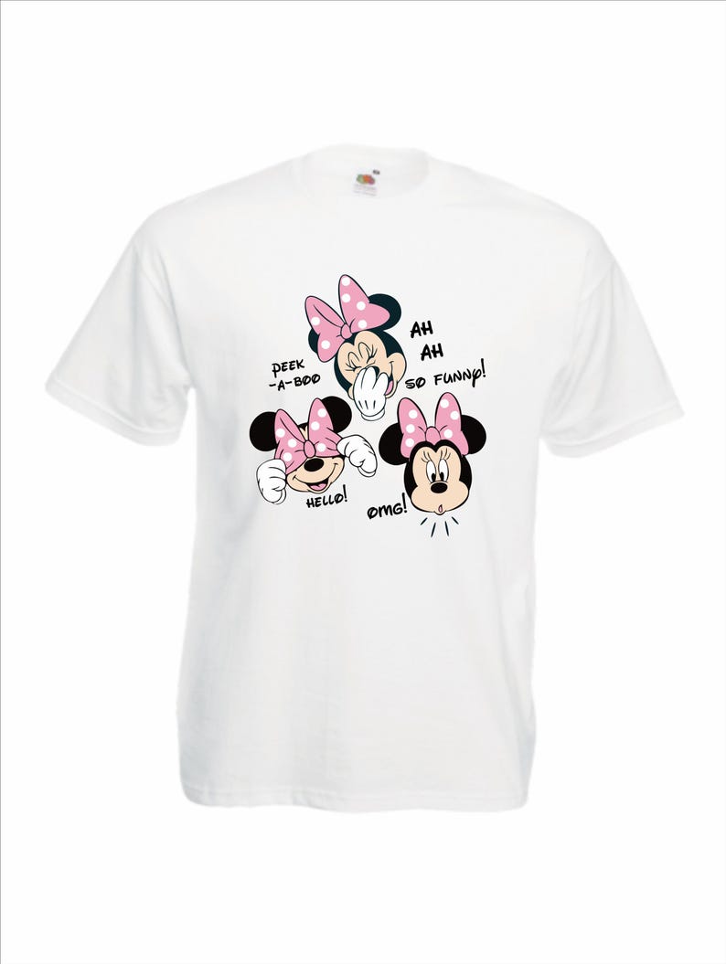 Op de afbeelding: Wit t-shirt met drie Minnie Mouse-gezichten met roze strikken. Tekst bevat "Peek-a-boo", "Hello!", "Ah Ah So Funny!" en "omg!". Het shirt is gemaakt van een zacht materiaal.