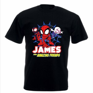 May include: A black short-sleeved t-shirt featuring a graphic of three cartoon spider-themed characters in front of a blue web. Below the characters, the text reads JAMES AND AMAZING FRIENDS in white and yellow block lettering on the chest.