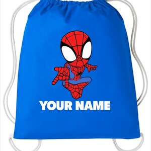 May include: A bright blue drawstring bag featuring a cartoon illustration of a red and blue superhero character with large white eyes. Below the character, the text YOUR NAME is printed in bold white capital letters. The bag has white cords.