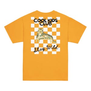 Peut inclure: T-shirt jaune moutarde avec un motif graphique au dos. Le motif présente une illustration de chat avec des accents floraux, sur un fond à carreaux blancs et beiges. Le texte "COOL KIDS CLUB" et "Stay Wild" est également inclus dans le design.