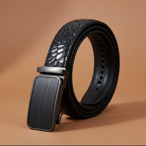 Op de afbeelding: Een zwarte leren riem met een textuur van slangenleer. De riem heeft een rechthoekige, gunmetal-kleurige gesp met een strak, modern design. De riem wordt getoond tegen een warme, neutrale achtergrond.