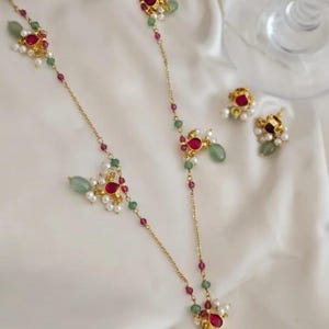 Könnte beinhalten: Ein goldfarbenes Schmuckset mit Halskette und Ohrringen. Die Halskette und die Ohrringe haben rote, grüne und weiße Akzente. Die Halskette hat eine zarte Kette mit dekorativen Elementen. Die Ohrringe haben ein ähnliches Design.