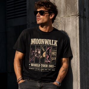 Puede incluir: Una camiseta negra de manga corta con un estampado gráfico que incluye el texto MOONWALK WORLD TOUR 1983. El diseño presenta cinco paneles verticales que muestran un horizonte urbano, una bola de discoteca, un vinilo, un bailarín y un radiocasete.