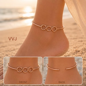 May include: A rose gold anklet featuring three interconnected circular rings as a central design element. The jewelry piece has an open-ended cuff style, visible from both the front with the rings and the back with the open gap. Text VVJ is present.