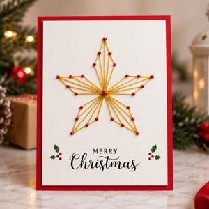 May include: A white rectangular greeting card with a red border featuring a gold string art star design created with small red beads. Below the star, the text Merry Christmas is printed in black, flanked by small green holly leaves and red berries.