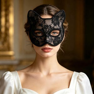 May include: A black lace cat mask featuring a floral rose pattern, scalloped edges, and thin wire whiskers. The mask covers the upper face, including the eyes, and includes a small black bead at the nose area to complete the feline appearance.