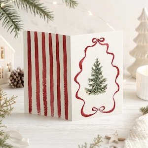 May include: A folded greeting card featuring a watercolour illustration of a green Christmas tree centred within a red ribbon frame on the right side, and vertical red stripes on the left side, set against a white textured paper background.