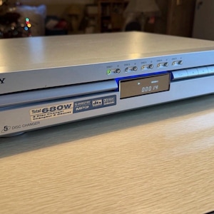 May include: Silver Sony 5-disc CD player. The device has a digital display showing the current track time. Features include S-Master, MP3, and DTS. The front panel has a 5-disc changer label and a power rating of 680W.