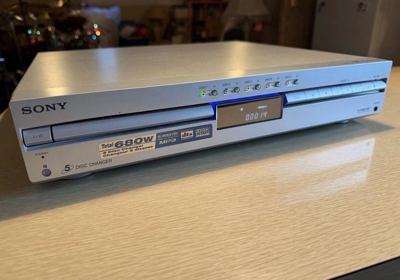 May include: Silver Sony 5-disc CD player. The device has a digital display showing the current track time. Features include S-Master, MP3, and DTS. The front panel has a 5-disc changer label and a power rating of 680W.
