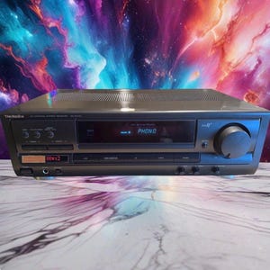 Puede incluir: Un receptor estéreo Technics AV Control modelo SA-EX110 de color negro. El panel frontal cuenta con una pantalla digital que muestra el texto PHONO y 100Wx2, una perilla de volumen circular grande a la derecha, varios botones y una toma de auriculares.