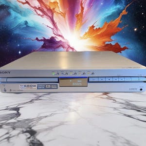 May include: Silver Sony DVD player with a digital display showing "00005". The player has several buttons and a slot for discs. The front of the player has the text "Total 680W" and "5 Disc Changer".