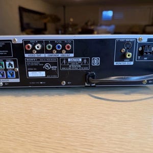 May include: Rear panel of a Sony DVD receiver with various input and output ports, including video, audio, and speaker connections. The panel has labels for Video/Sat, Component Video Out, and Monitor Out. A power cord is connected.